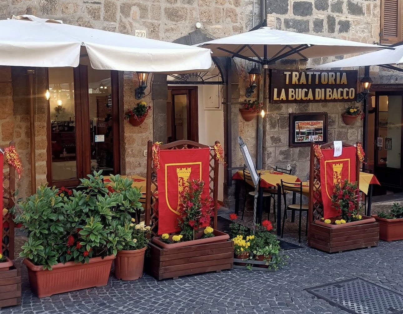 L'ingresso della Trattoria La Buca di Bacco lungo Corso Cavour a Orvieto, con i tavoli all'aperto e gli stendardi della città